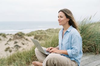 Femme assise en extérieur face à la mer avec ordinateur